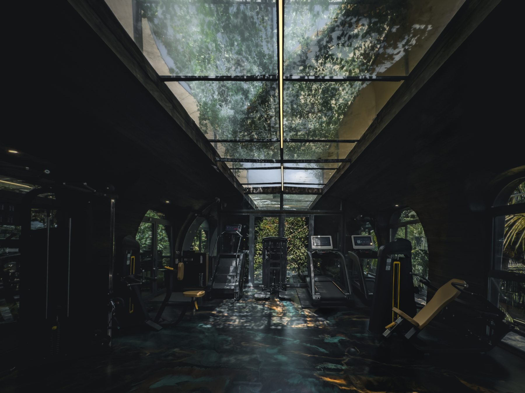 Machine hall under a glass roof, treadmills and machines facing the jungle